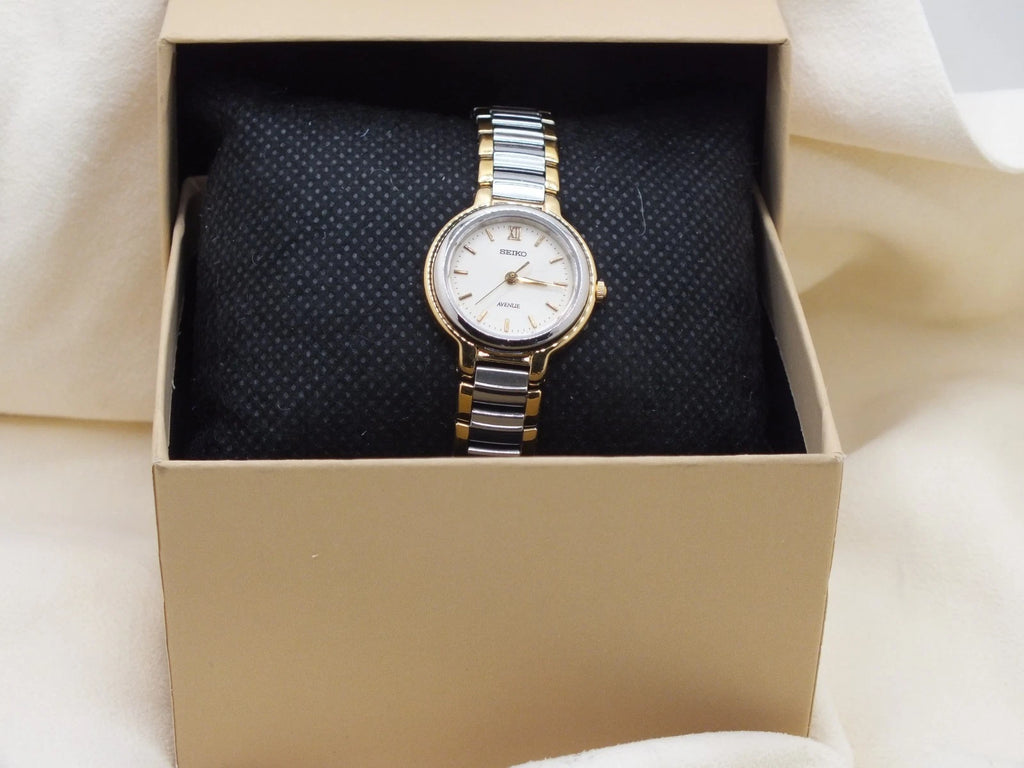 Seiko Avenue 1F21-0H50 ladies’ quartz two-tone watch with gold accents, white dial, and linked metal band displayed in a beige box.