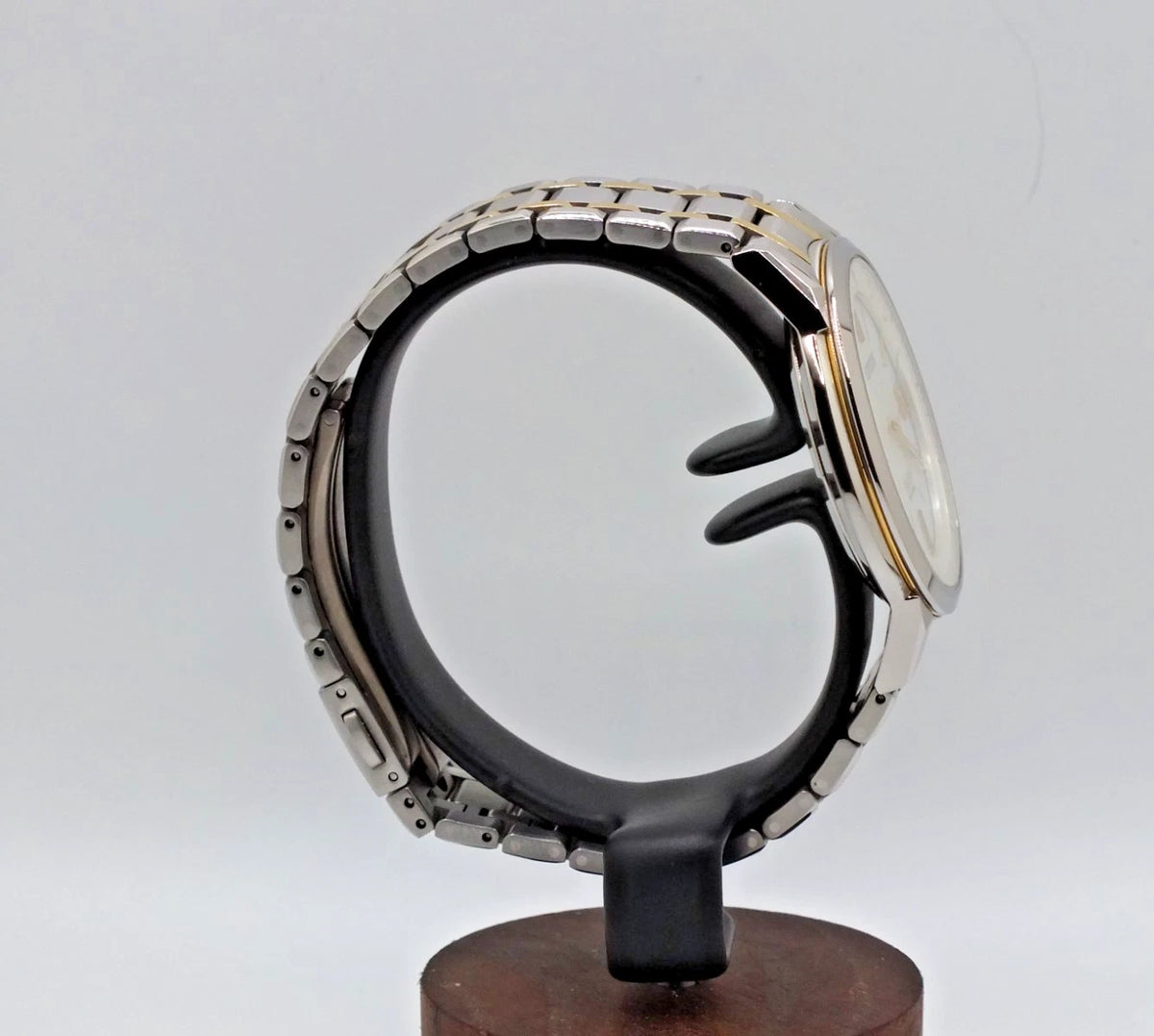 Silver and titanium two-tone Citizen Exceed H113 Eco-Drive radio watch with black strap and gold case on wooden display stand.