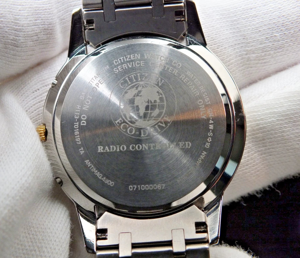 Back of Citizen Exceed H113 Eco-Drive Radio Titanium Two-Tone watch with gold text and blue Earth graphic on black dial.