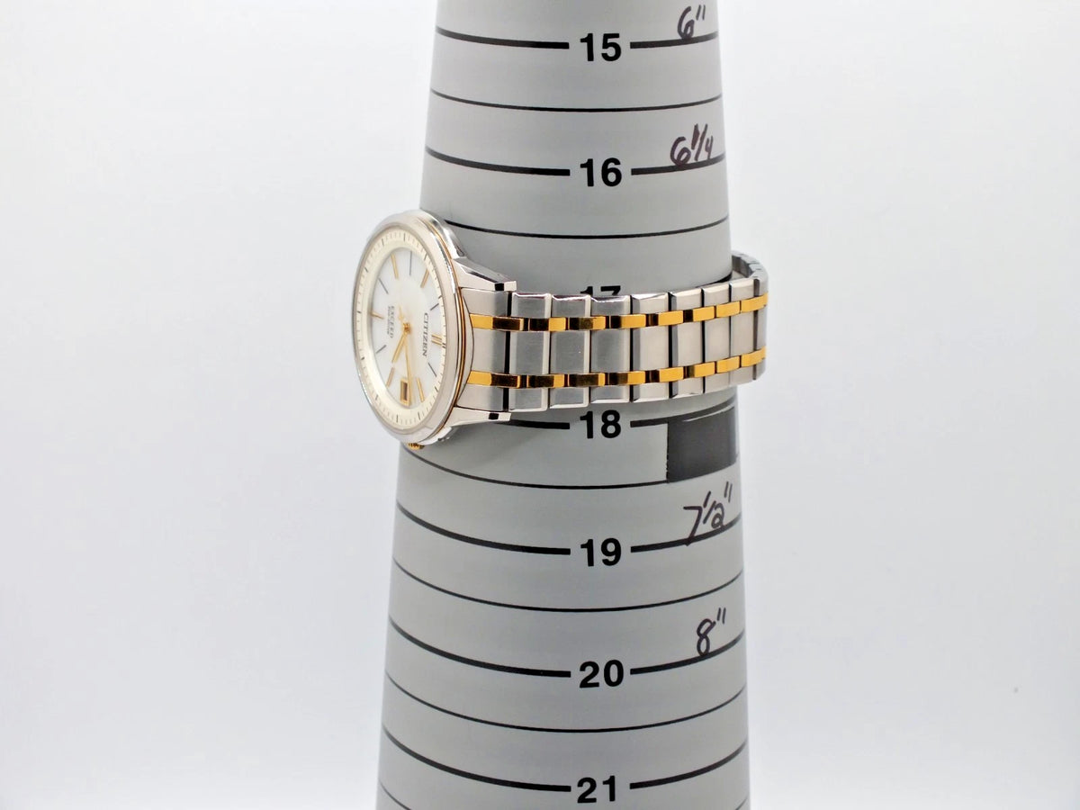 Silver and black two-tone Citizen Exceed H113 Eco-Drive watch with gold dial, displayed on marked wrist height chart.