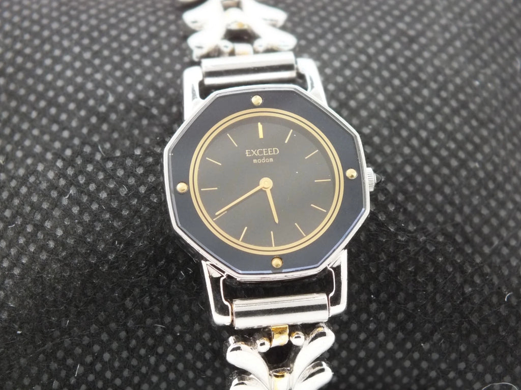 Silver-tone vintage Citizen Exceed women’s quartz black dial bracelet with gold hour markers and linked metal band.