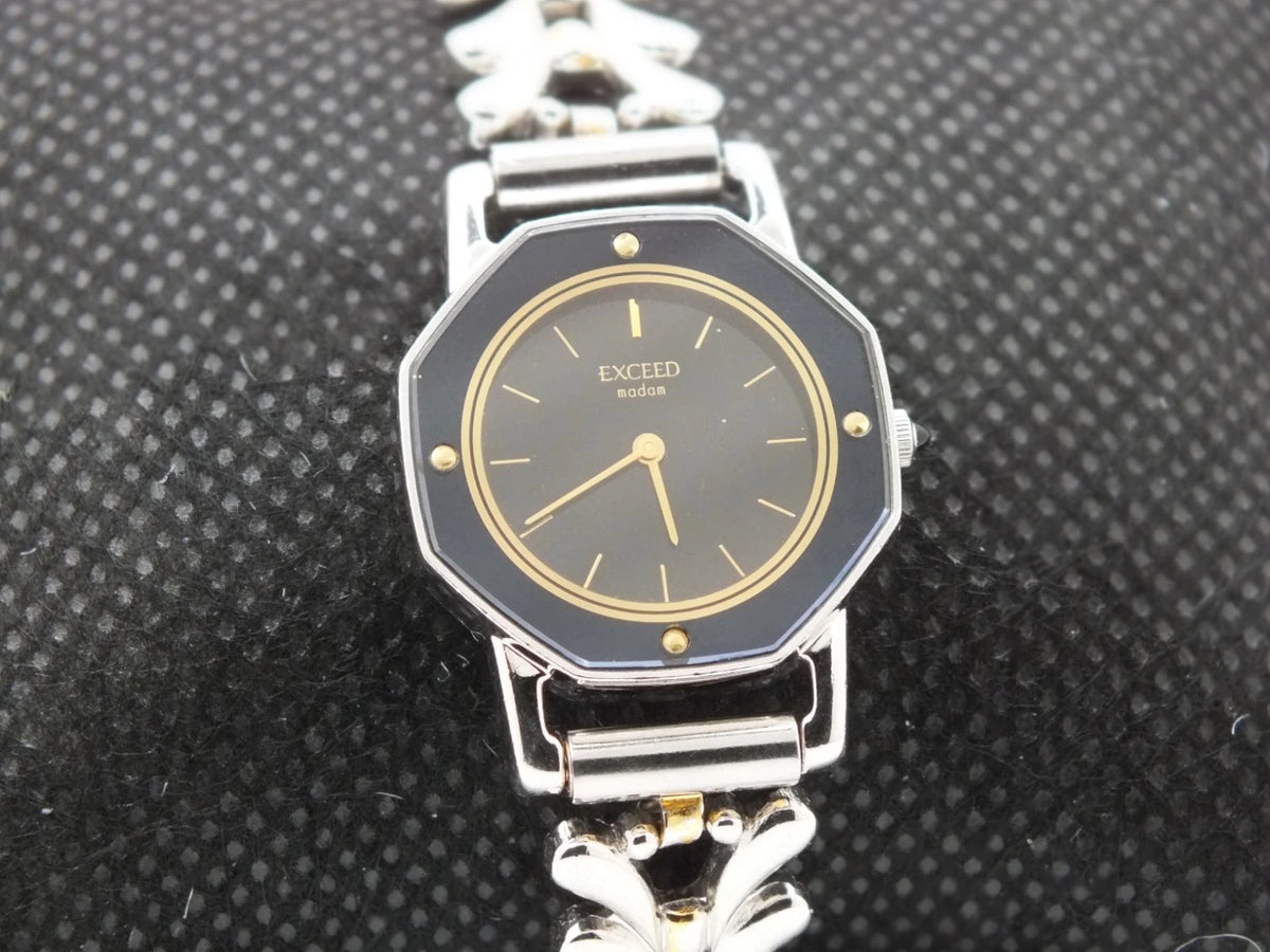 Silver-tone vintage Citizen Exceed women’s quartz black dial bracelet with gold hour markers and linked metal band.
