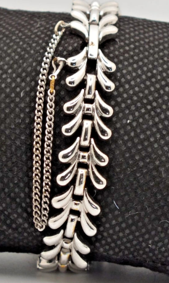Silver chain bracelet with curved leaf-shaped connectors and two white pearl dials on a textured black background.