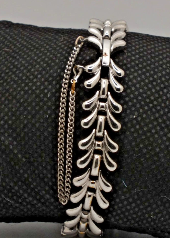 Silver chain bracelet with curved leaf-shaped connectors and two small gold accents, displayed on a textured black surface.